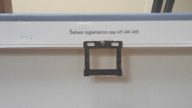 May include: Close-up of the back of a canvas art piece. The canvas is white with a light blue border. A metal hanger is attached to the back. The text "Sabam registration cae 471 481 452" is printed on the canvas.