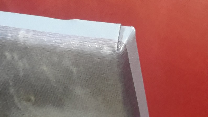 May include: Close-up of a corner of a light gray object with a textured surface. The object has a white border and is set against a red background. The corner is sharply angled.