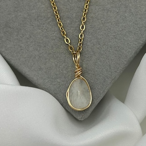 May include: A gold chain necklace with a white gemstone pendant wrapped in gold wire.