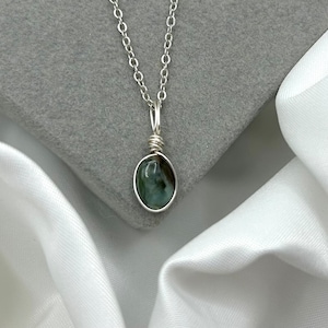 May include: A silver chain necklace with a green gemstone pendant. The pendant is wrapped in silver wire.