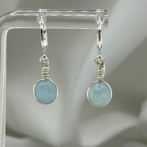 May include: A pair of silver earrings featuring light blue aquamarine stones. The earrings are crafted with wire wrapped around the stones and have a lever back fastening.