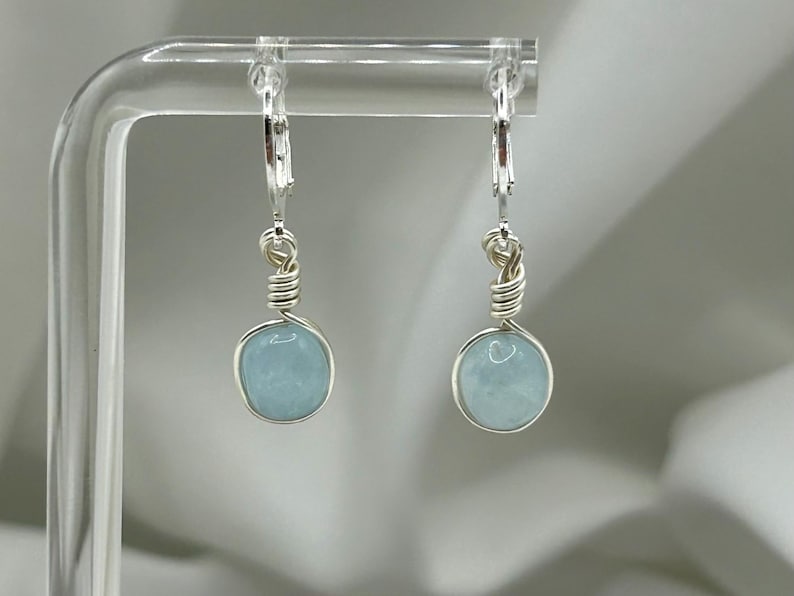 May include: A pair of silver earrings featuring light blue aquamarine stones. The earrings are crafted with wire wrapped around the stones and have a lever back fastening.