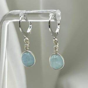 May include: A pair of silver hoop earrings with light blue aquamarine stones hanging from them.