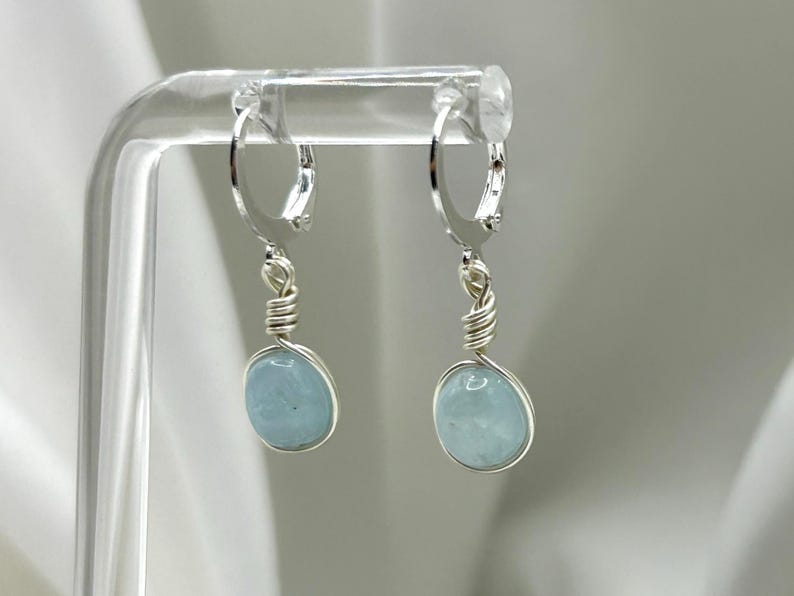 May include: A pair of silver hoop earrings with light blue aquamarine stones hanging from them.