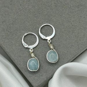 May include: A pair of silver hoop earrings with light blue oval-shaped stones hanging from them.