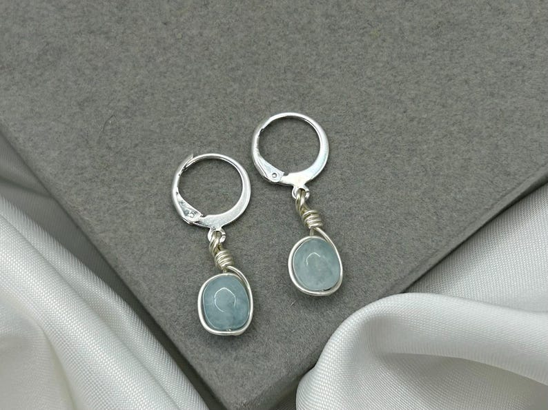 May include: A pair of silver hoop earrings with light blue oval-shaped stones hanging from them.