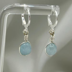 May include: A pair of silver earrings featuring light blue aquamarine stones. The earrings have a simple wire design and are ideal for everyday wear.