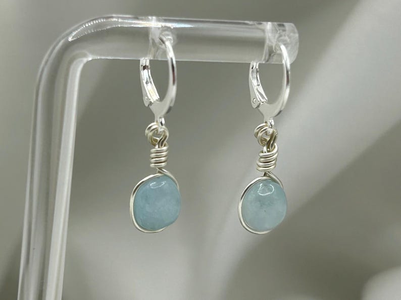 May include: A pair of silver earrings featuring light blue aquamarine stones. The earrings have a simple wire design and are ideal for everyday wear.