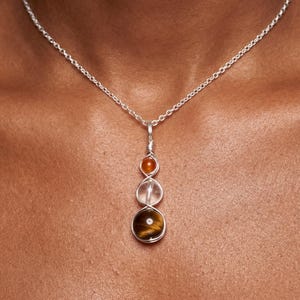 May include: A silver pendant necklace with three gemstone beads: an orange bead, a clear pink bead, and a brown tiger's eye bead. The beads are wire-wrapped and hang from a fine silver chain.