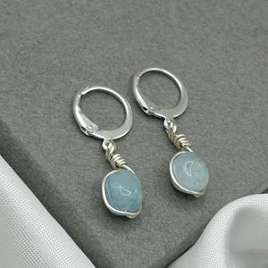 May include: A pair of silver hoop earrings with a light blue gemstone dangling from each hoop.