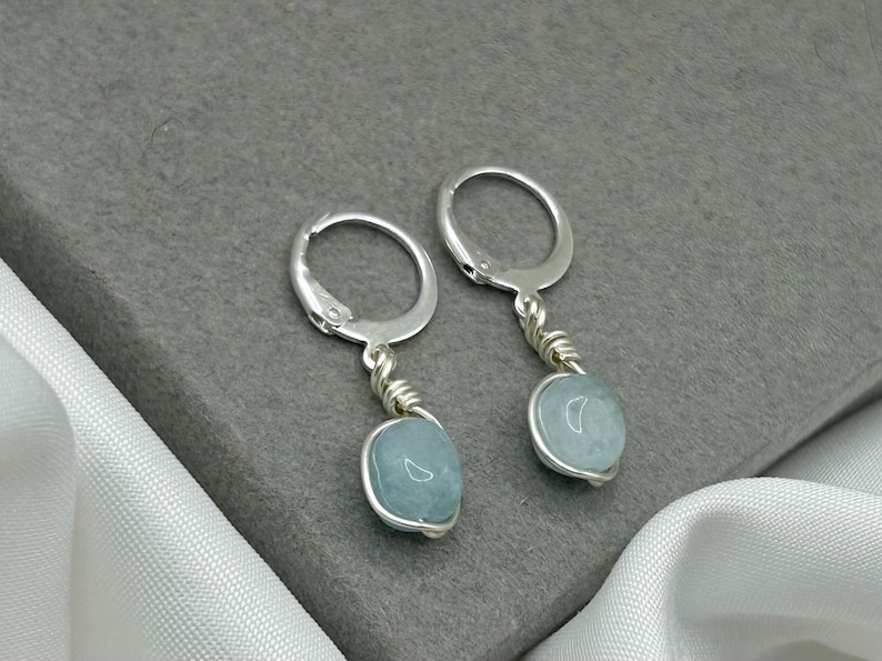 May include: A pair of silver hoop earrings with a light blue gemstone dangling from each hoop.