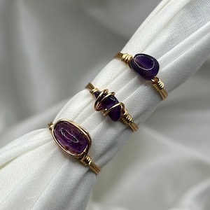 May include: Three gold rings with amethyst stones. The rings are wrapped in gold wire and feature different shapes and sizes of amethyst.