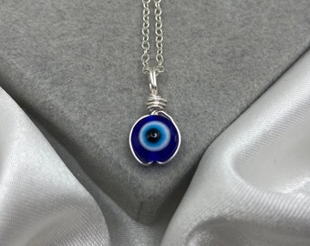 Peut inclure: Un collier en chaîne argent avec un pendentif en forme d'œil bleu maléfique. Le pendentif est entouré de fil d'argent.