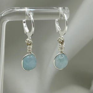May include: A pair of silver hoop earrings with light blue aquamarine stones hanging from them.