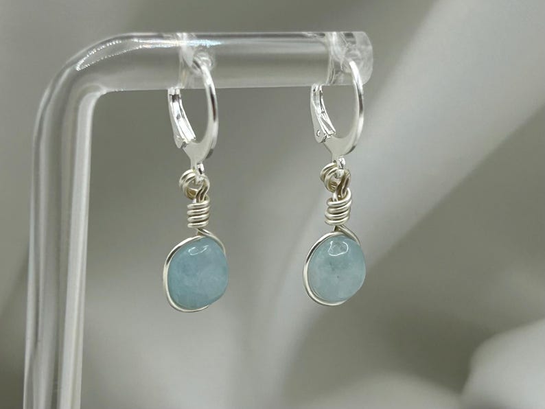 May include: A pair of silver hoop earrings with light blue aquamarine stones hanging from them.