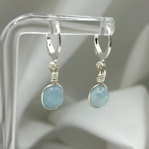 May include: A pair of silver hoop earrings with light blue aquamarine stones hanging from them.