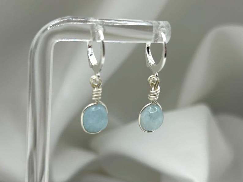 May include: A pair of silver hoop earrings with light blue aquamarine stones hanging from them.