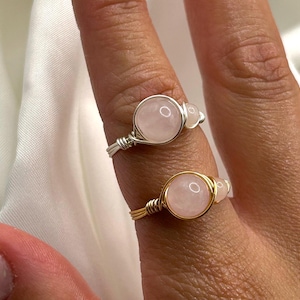 May include: Two rings featuring pink rose quartz stones wrapped in silver and gold wire.