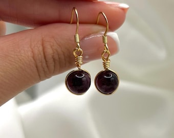 Puede incluir: Un par de pendientes colgantes de oro con cuentas de piedras preciosas de color morado oscuro.
