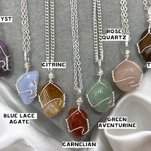 May include: Seven silver necklaces with different coloured gemstone pendants. The pendants are wrapped in silver wire. The gemstones are amethyst, blue lace agate, citrine, carnelian, green aventurine, rose quartz, and tiger's eye.