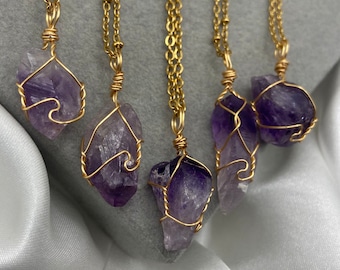 May include: Five gold chain necklaces with amethyst crystal pendants wrapped in gold wire. The amethyst crystals are various shapes and sizes.