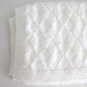 May include: White knitted baby blanket with a diamond pattern.