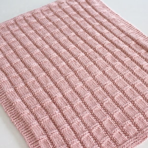Puede incluir: Una suave manta de bebé de punto rosa con un patrón de punto de waffle texturizado.