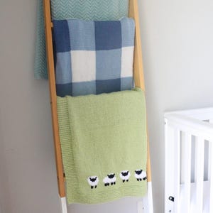 Pu&ograve; includere: Una scala di legno espone tre coperte lavorate a maglia. La coperta superiore &egrave; verde acqua chiaro con un motivo a spina di pesce. La coperta centrale &egrave; a quadri blu e bianchi. La coperta inferiore &egrave; verde chiaro con pecore.