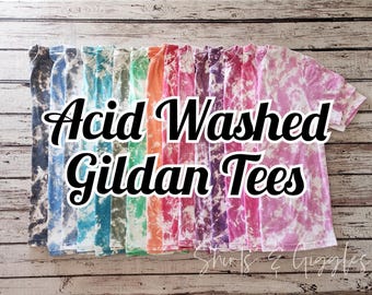 May include: A collection of short-sleeved t-shirts featuring an acid-washed tie-dye pattern in various colours including blue, green, orange, pink, and purple. The text Acid Washed Gildan Tees is overlaid in black script across the centre of the shirts.