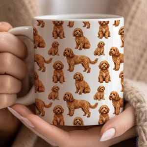 May include: White ceramic mug with a repeating pattern of brown and tan dog illustrations. The dogs are shown in different poses, such as sitting and standing. The mug has a white handle and is held by a person.