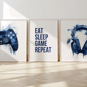 Pode incluir: Três impressões emolduradas com um efeito de aquarela azul. A impressão da esquerda apresenta um controlador de videogame azul, a impressão do meio tem o texto "EAT SLEEP GAME REPEAT", e a impressão da direita mostra um fone de ouvido azul.