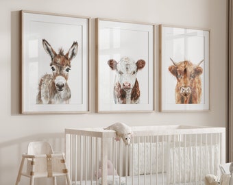 May include: Three framed animal prints in a nursery setting. The prints feature a donkey, a cow, and a bull. The prints are hung above a white crib with a white mattress and a white crib bumper. There are stuffed animals and a basket on the floor.