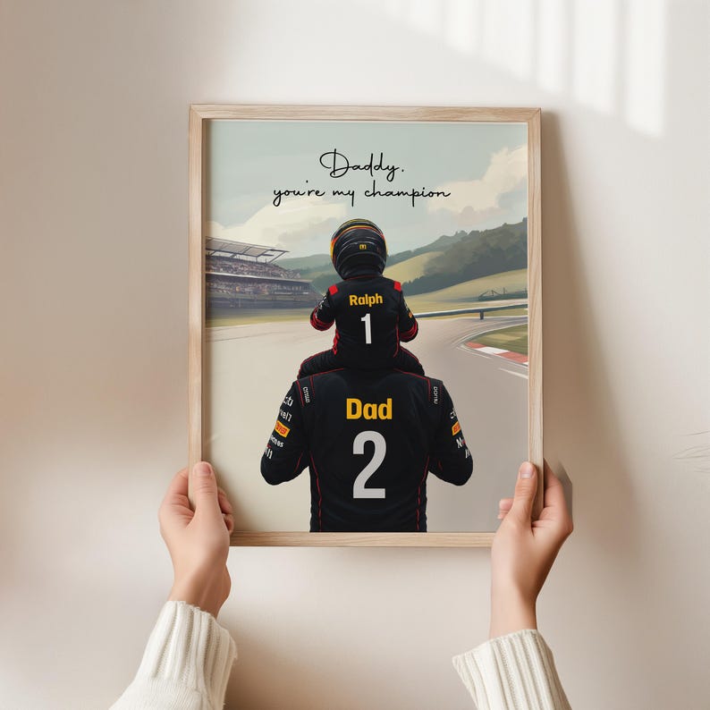 May include: A framed print featuring a child in a racing suit with the name Ralph and number 1 sitting on the shoulders of an adult in a racing suit with the word Dad and number 2, with the text Daddy, you're my champion on a racetrack background.