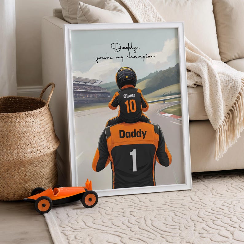 May include: A framed print featuring an illustration of a person wearing a black and orange racing suit with the number 1 and the word Daddy on the back, carrying a child in a racing suit with the number 10 and the name Oliver. Text reads: Daddy. you're my champion.