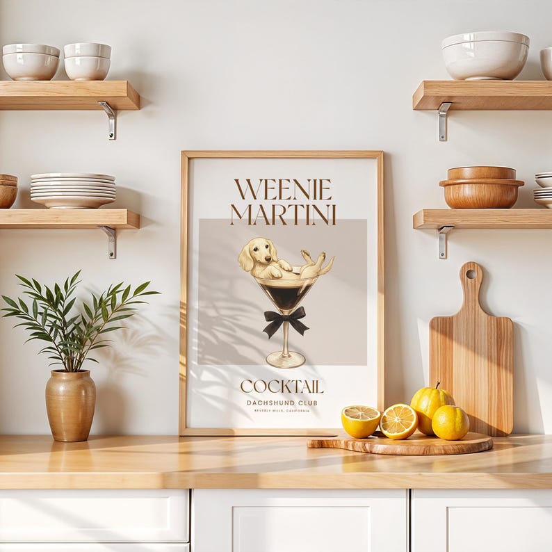 May include: A framed print featuring a dachshund dog in a martini glass, with the words "Weenie Martini" above and "Cocktail Dachshund Club" below. The artwork has a light brown and beige color scheme, with a black bow tie on the glass.