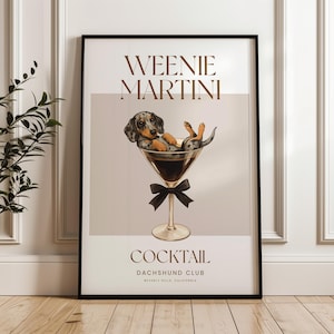 May include: A framed art print featuring a dachshund dog relaxing in a martini glass. The print has the words "Weenie Martini" and "Cocktail Dachshund Club" in a stylish font. The dog is black, brown, and gray.