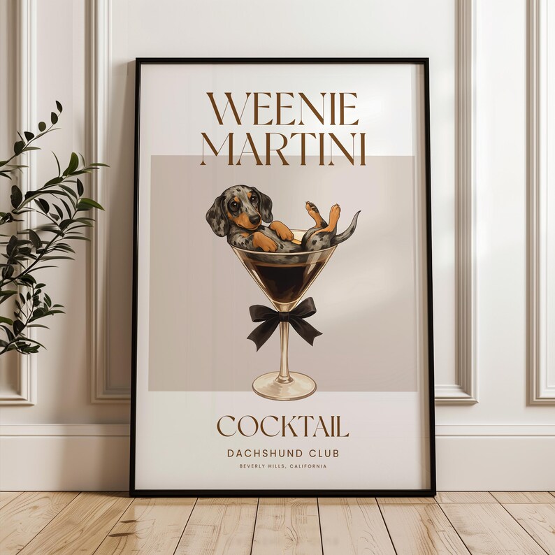 May include: A framed art print featuring a dachshund dog relaxing in a martini glass. The print has the words "Weenie Martini" and "Cocktail Dachshund Club" in a stylish font. The dog is black, brown, and gray.