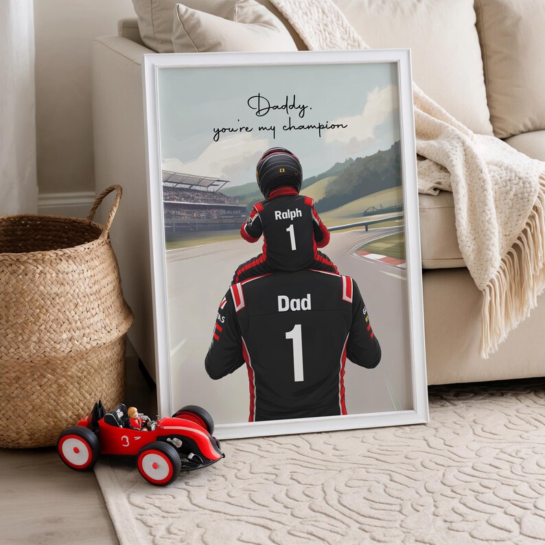 May include: A framed digital illustration showing a child wearing a racing suit and helmet sitting on the shoulders of an adult in a matching racing suit. The text reads, "Daddy, you're my champion," with "Ralph" and "1" on the child's back.
