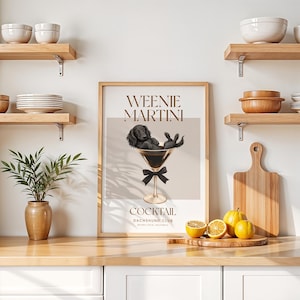 May include: A framed print with the words "Weenie Martini Cocktail Dachshund Club" features a black dachshund dog relaxing in a martini glass. The print has a neutral color palette with a black bow at the base of the glass.
