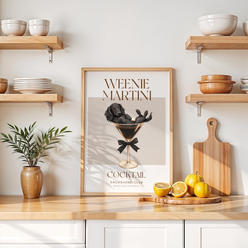 May include: A framed print with the words "Weenie Martini Cocktail Dachshund Club" features a black dachshund dog relaxing in a martini glass. The print has a neutral color palette with a black bow at the base of the glass.