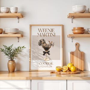 May include: A framed print featuring a dachshund dog and a rabbit in a martini glass, with the words "Weenie Martini" and "Cocktail" in brown text. The print is displayed on a wooden countertop with lemons and a cutting board.