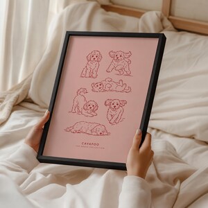 May include: A black framed print featuring six dark red line art illustrations of Cavapoo dogs in various poses on a dusty rose background. The text at the bottom reads CAVAPOO THE BREED COLLECTION in a simple, clean, sans-serif font.