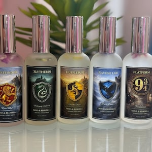 May include: Five glass spray bottles with silver tops, each labeled with a different house crest from a fantasy series. The bottles are filled with colored liquid and the labels read: Gryffindor, Slytherin, Hufflepuff, Ravenclaw, and Platform 9 3/4.