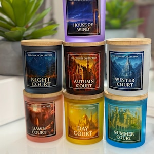 May include: A stack of seven glass candles with wooden lids. Each candle has a different color and label with the text "The Courts Collection" and a court name: House of Wind, Night Court, Autumn Court, Winter Court, Dawn Court, Day Court, and Summer Court.