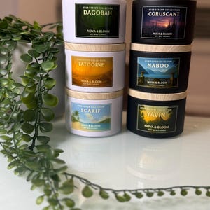 May include: A stack of six soy wax candles with wooden lids. The candles are labeled with the names of planets and locations from a science fiction franchise. The labels include the text "Star System Collection" and "Nova & Bloom Soy Wax Candle."