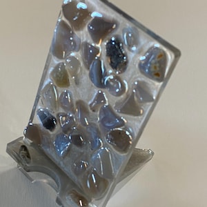May include: A clear acrylic phone stand with a decorative panel featuring a mosaic of small, gray and white stones.
