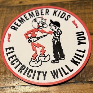 May include: A round, white sticker with a red border. The sticker features a black and white illustration of a devil character holding a knife and a boy. The text "Remember Kids Electricity Will Kill You" is written around the edge of the sticker.