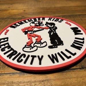 May include: A white round patch with a red border. The patch has a black and white illustration of two figures. The text "Remember Kids Electricity Will Kill You" is written around the figures.
