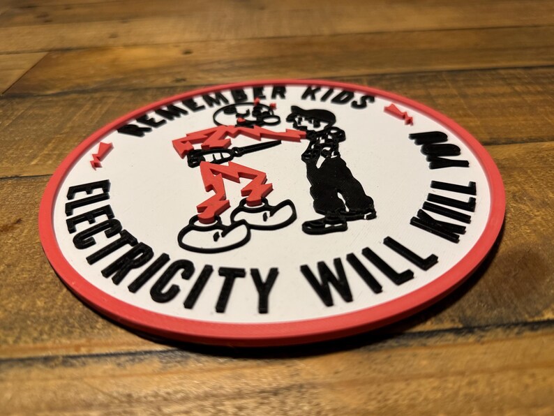 May include: A white round patch with a red border. The patch has a black and white illustration of two figures. The text "Remember Kids Electricity Will Kill You" is written around the figures.