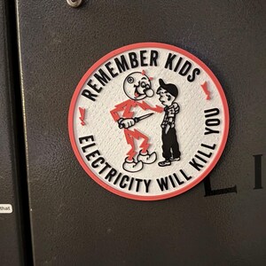May include: A red and white round sticker with the text "Remember Kids Electricity Will Kill You". A cartoon figure of a red devil holding a knife is shown next to a boy.